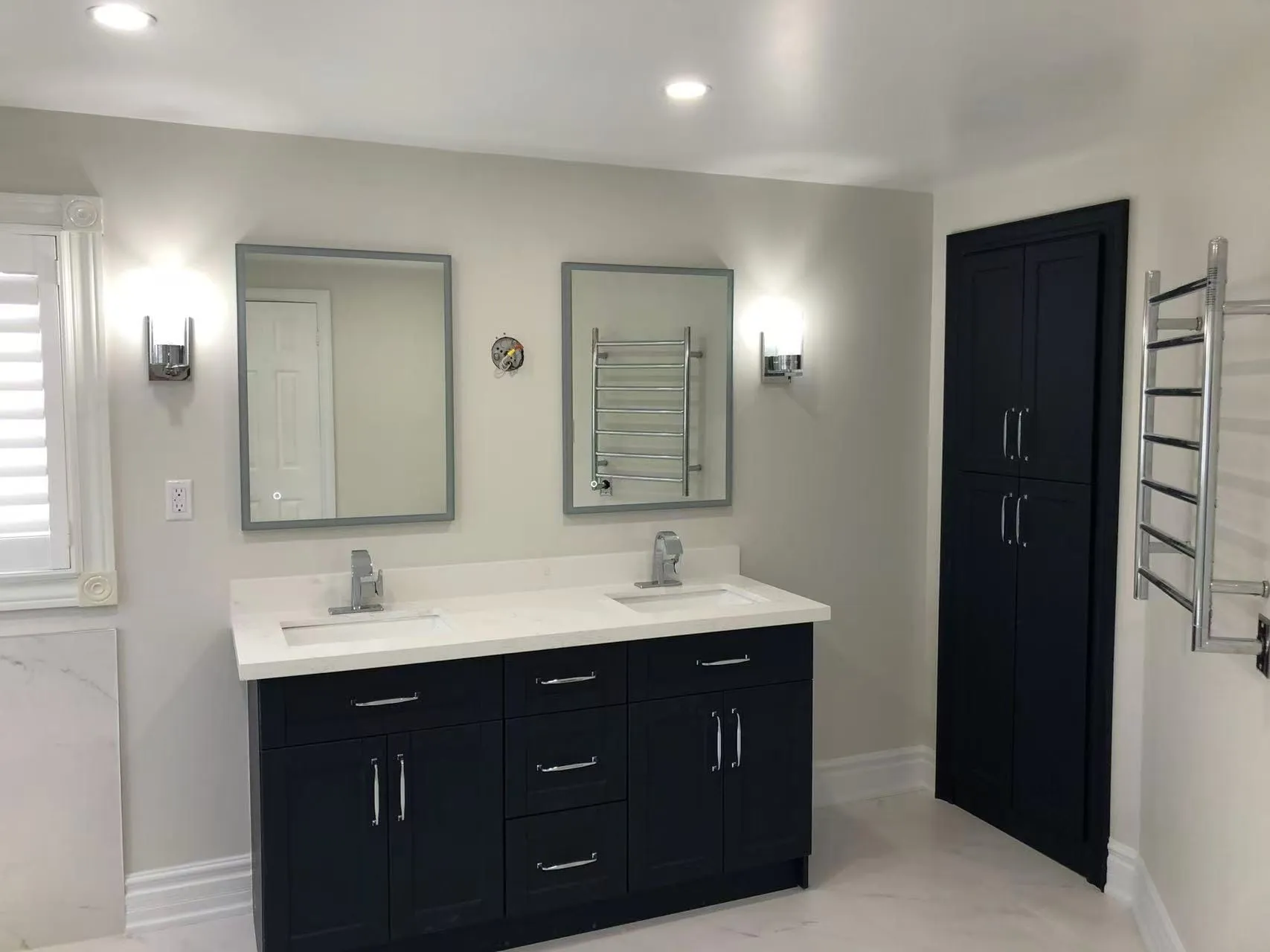 A navy double vanity with a white stone top, two backlit mirrors, wall sconces and a matching linen cabinet.