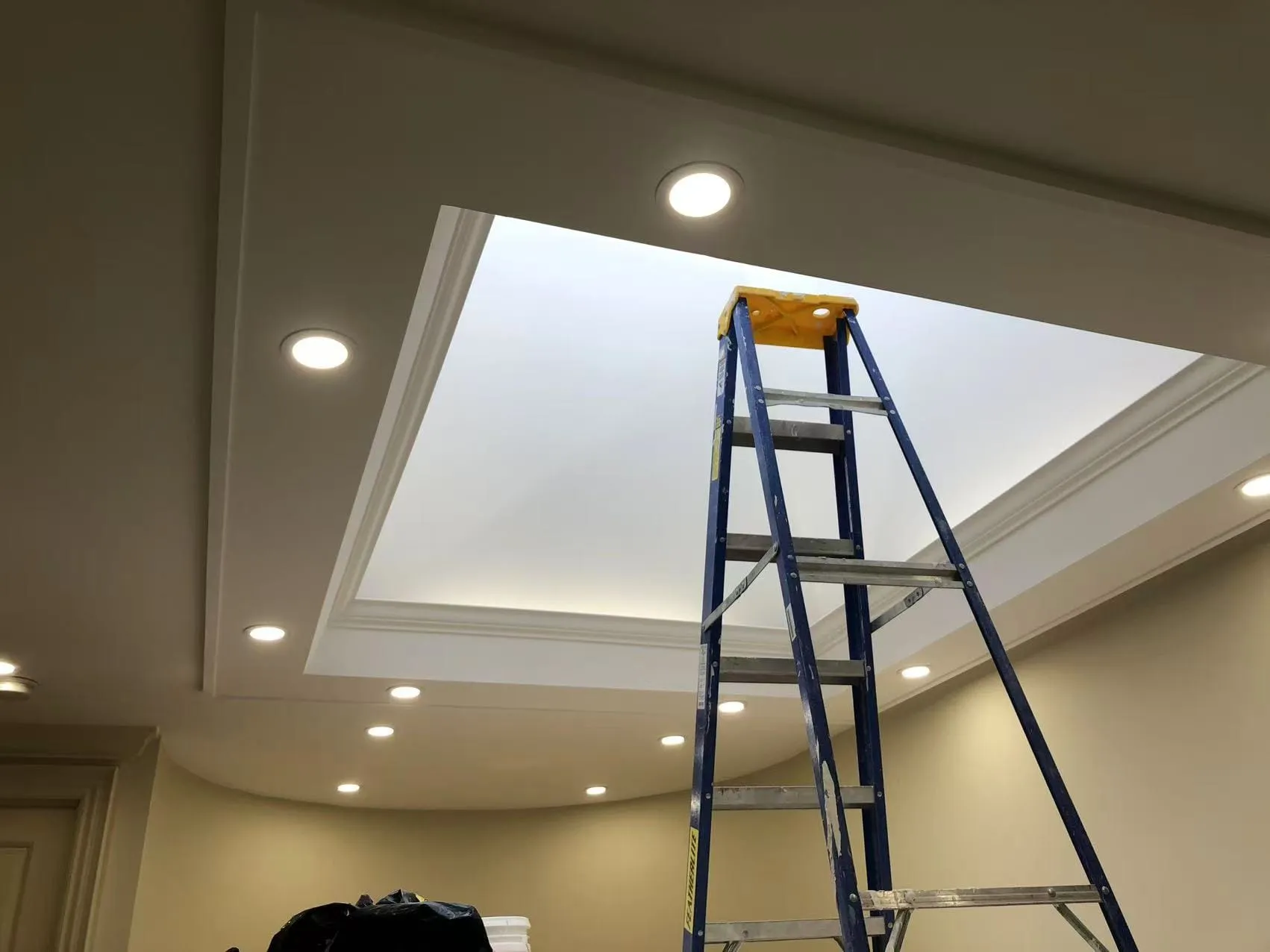The finished tray ceiling around the skylight, painted, with pot lights on.