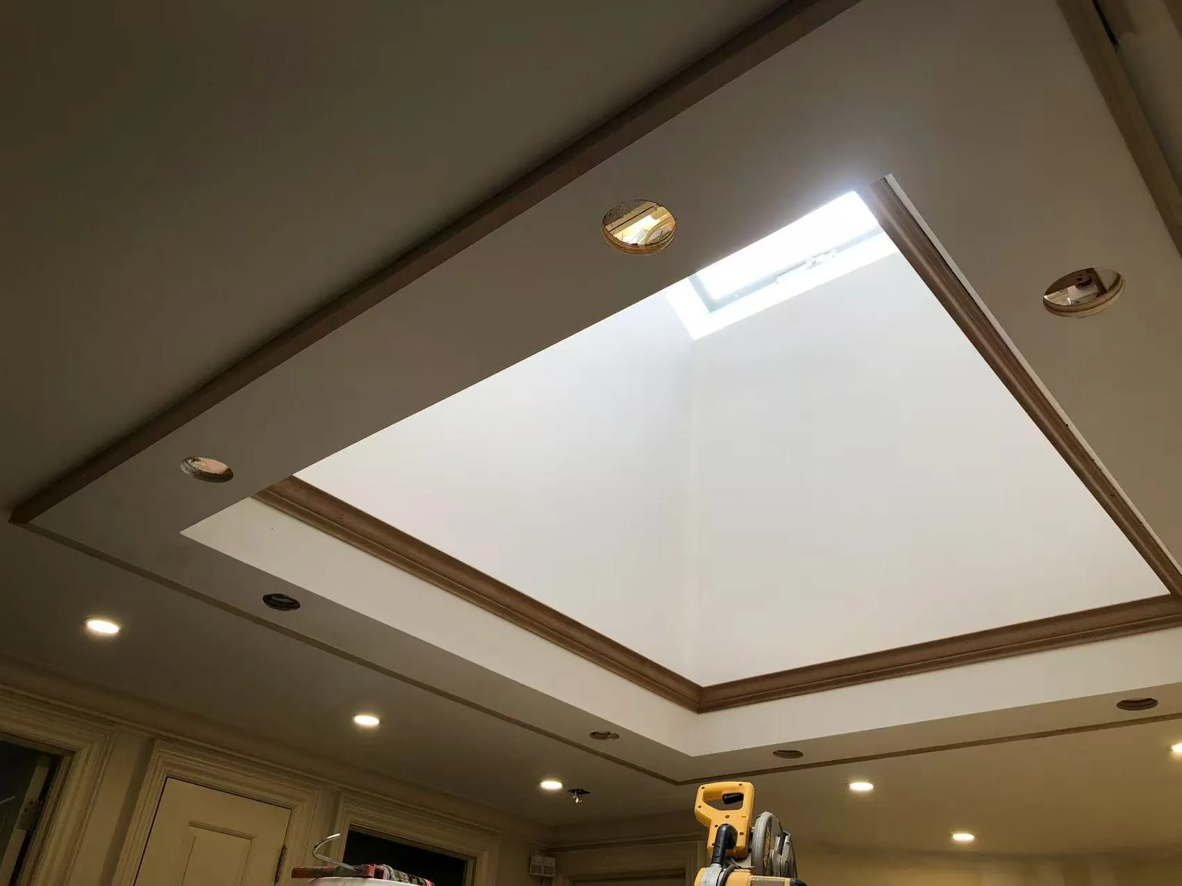A tray ceiling around a skylight during construction, with cut-outs for pot lights and unpainted trim.