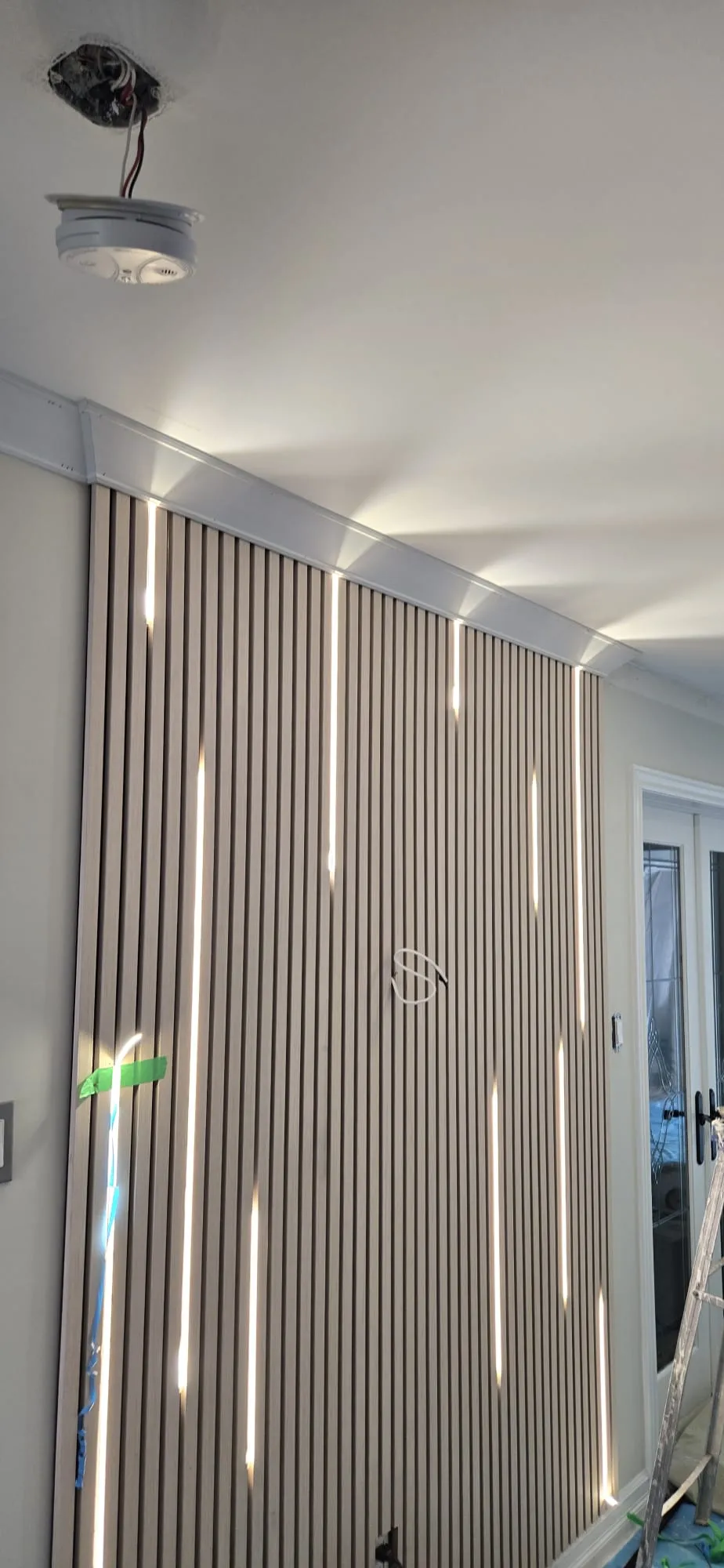 A slatted wood wall with built-in light strips during installation, wiring still exposed.